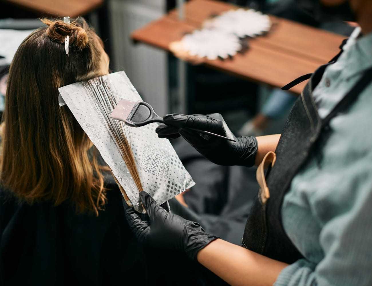 Hairdresser applying color to client's hair with a brush and foil for highlights.