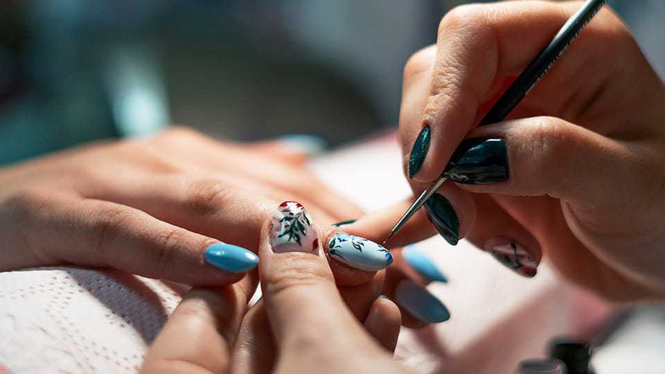 Person applying intricate floral nail art design on blue manicured nails.