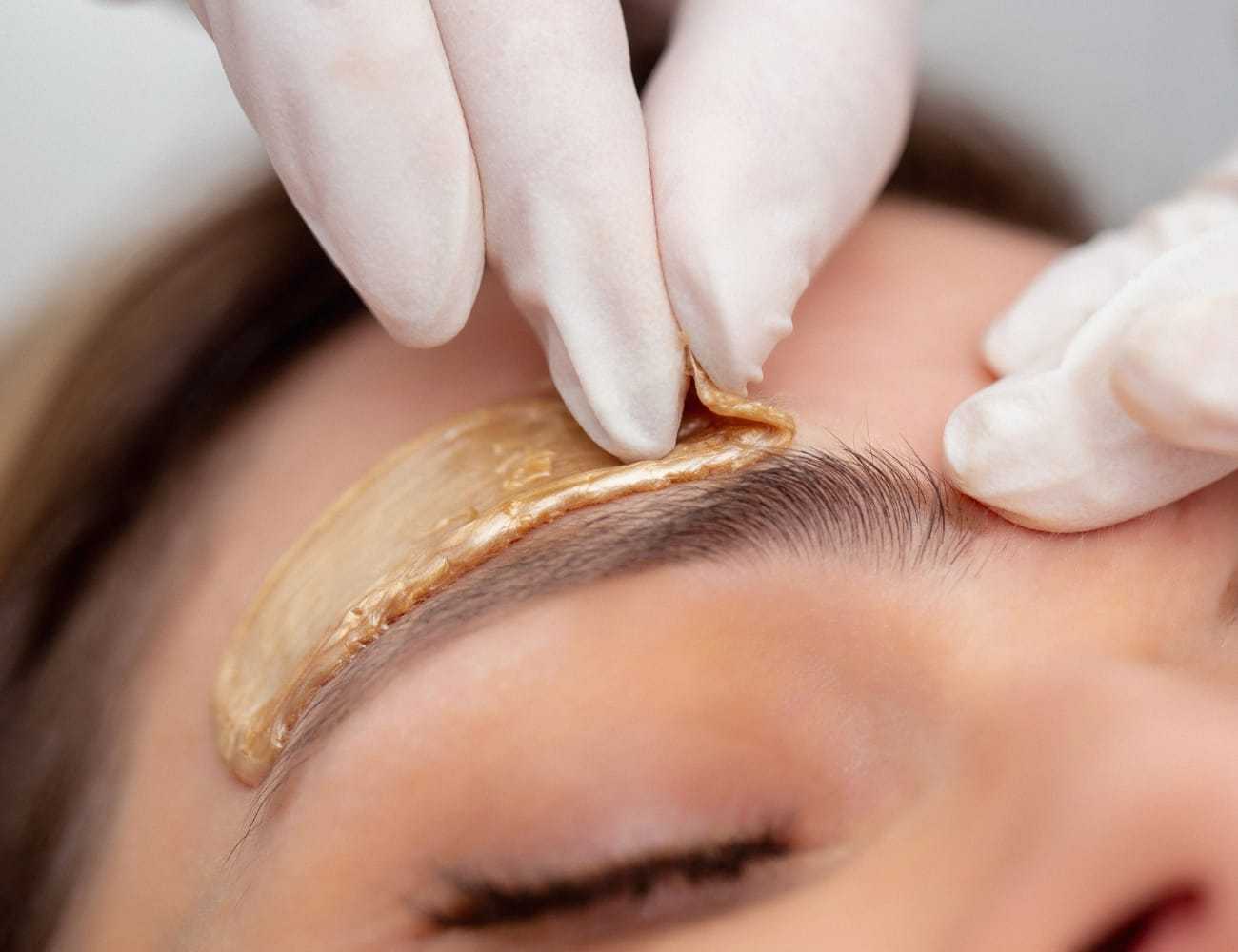 Eyebrow being shaped with wax by a professional wearing gloves.