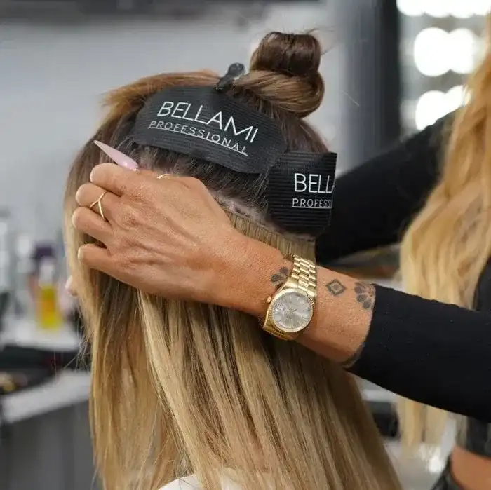 Hair stylist attaching extensions in a salon using Bellami products. Close-up of the process.