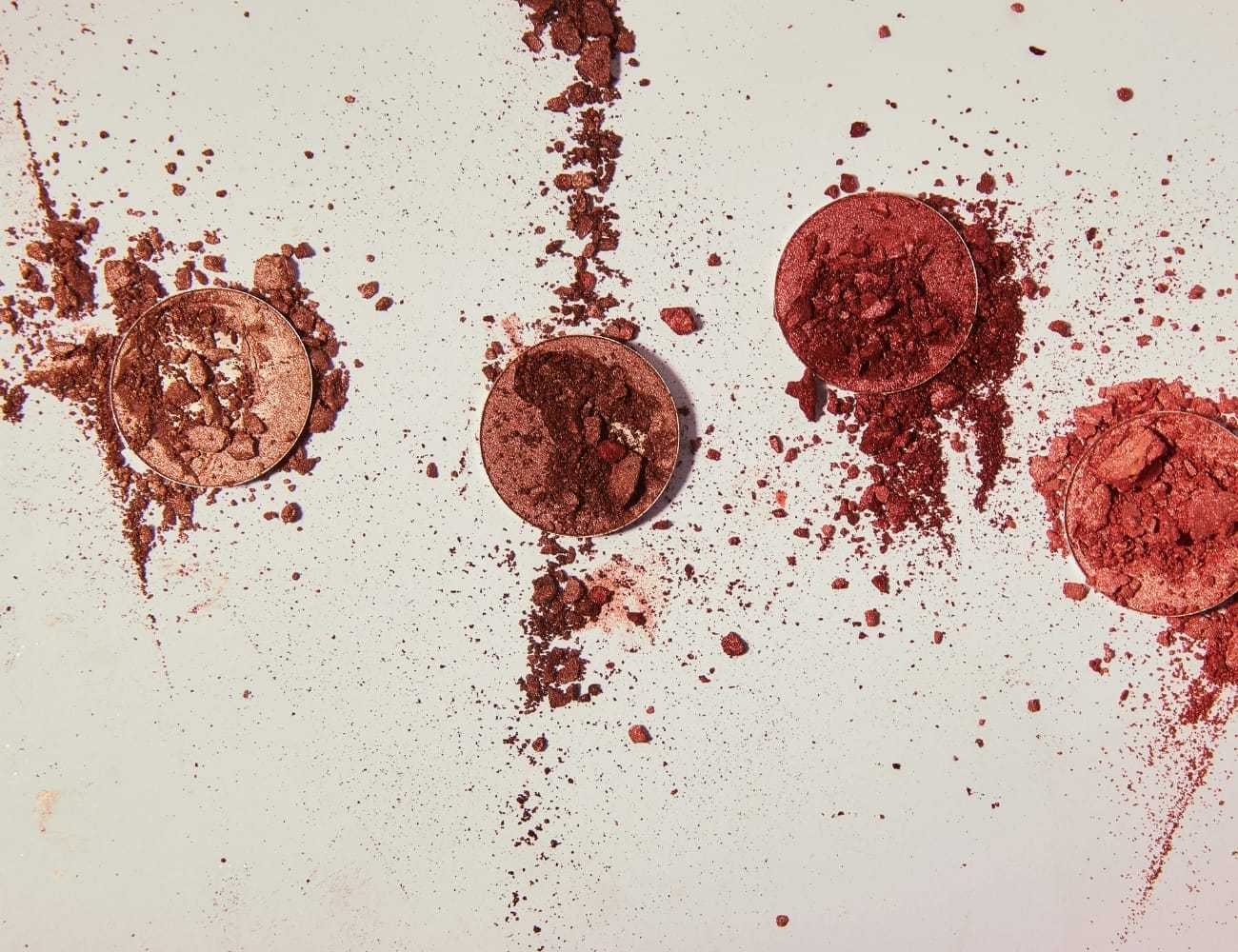 Broken eyeshadow palettes in various shades scattered on a white surface.
