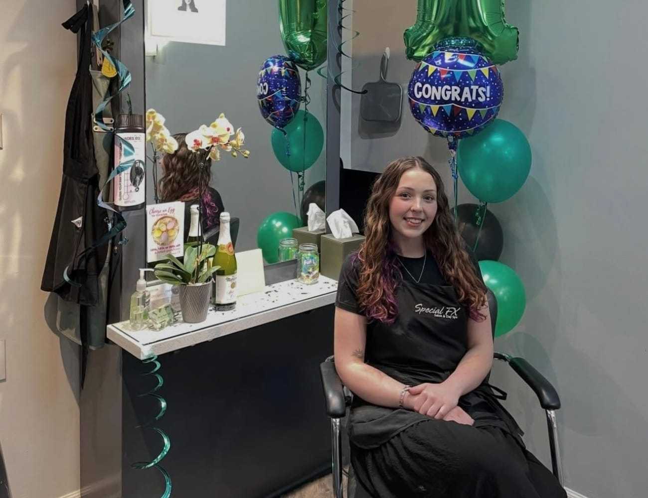 Young woman at a salon chair, surrounded by celebratory balloons and champagne.